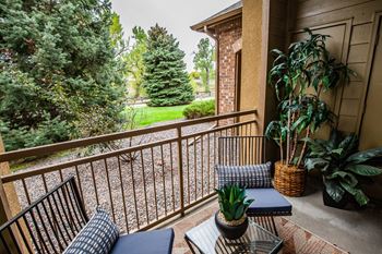 A balcony with a bench, potted plants, and a view of a lawn and trees.